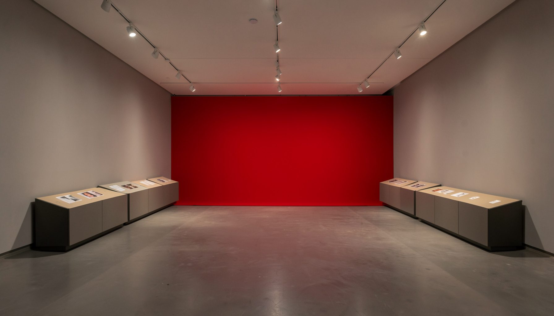 Wide-angle exhibition hall view with neutral gray walls, warm overhead lighting, and display panels arranged across the floor